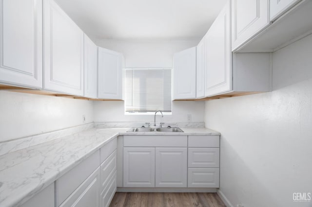 kitchen with light wood finished floors, white cabinets, and a sink