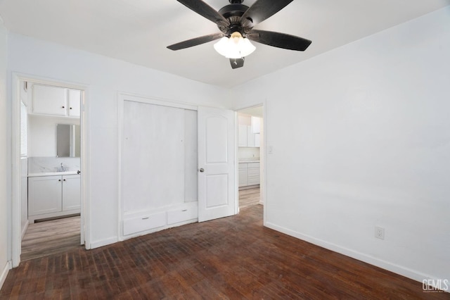 unfurnished bedroom featuring ceiling fan, dark wood-style flooring, a sink, baseboards, and a closet