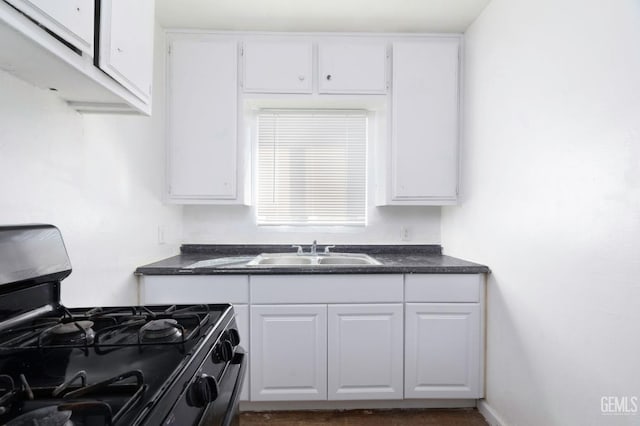 kitchen with dark countertops, white cabinetry, black gas stove, and a sink