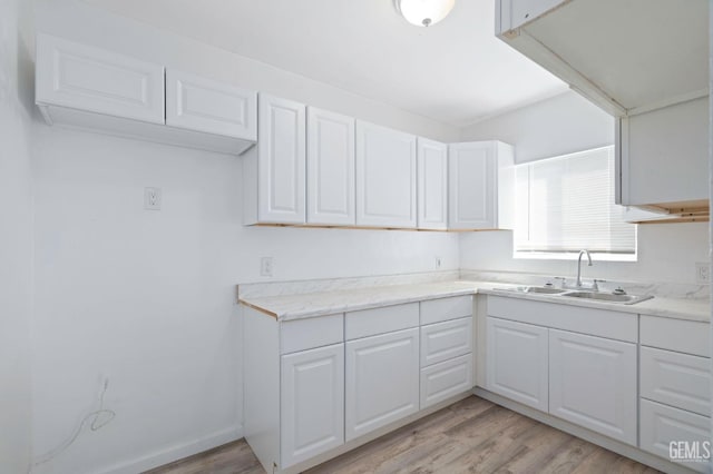 kitchen with light wood-type flooring, white cabinetry, and a sink