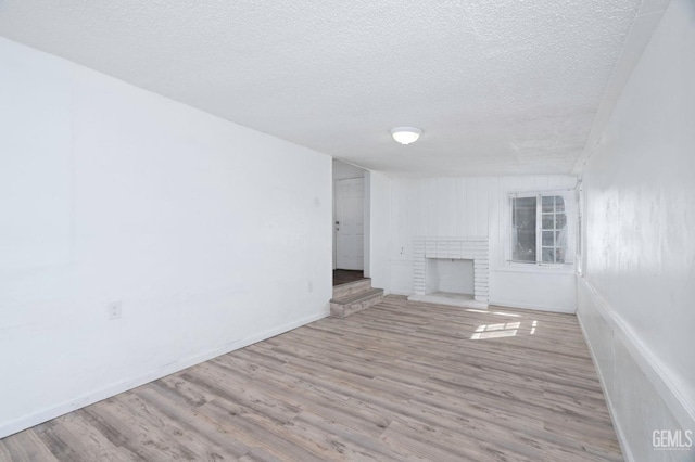 unfurnished living room with a textured ceiling, a fireplace, wood finished floors, and baseboards