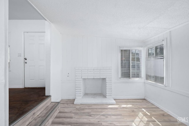 unfurnished living room with a textured ceiling, a fireplace, baseboards, and wood finished floors