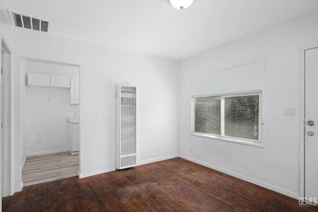 unfurnished bedroom with a heating unit, visible vents, baseboards, and wood finished floors