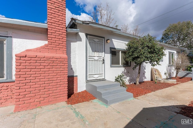 entrance to property featuring a chimney and stucco siding