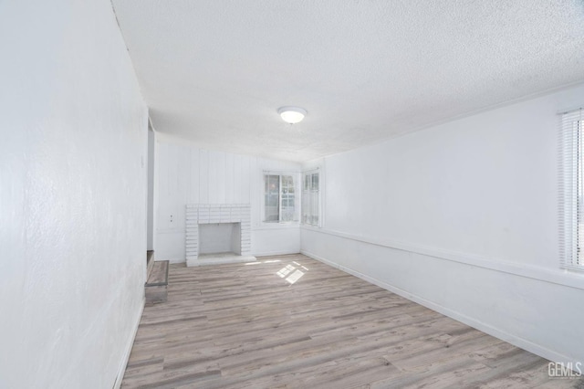 unfurnished living room with a brick fireplace, a textured ceiling, baseboards, and wood finished floors