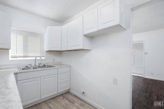 kitchen with a sink, white cabinetry, baseboards, light wood-style floors, and light countertops