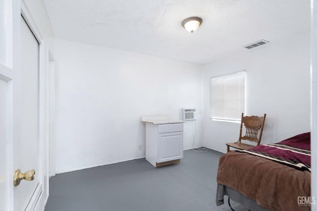 bedroom with concrete floors, visible vents, a textured ceiling, and an AC wall unit