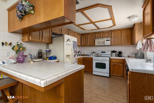 kitchen featuring a peninsula, white appliances, backsplash, and brown cabinets