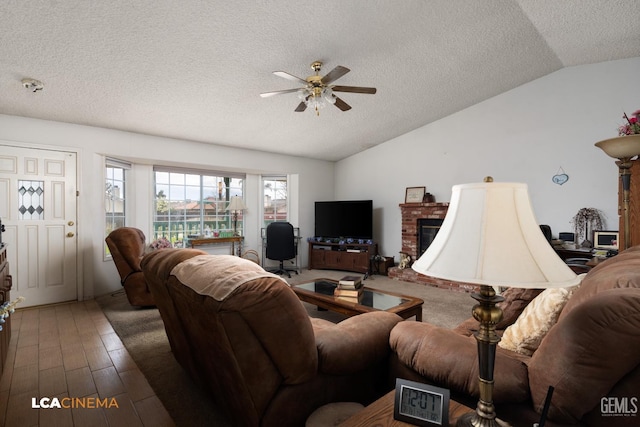 living room featuring a textured ceiling, a fireplace, wood finished floors, a ceiling fan, and vaulted ceiling