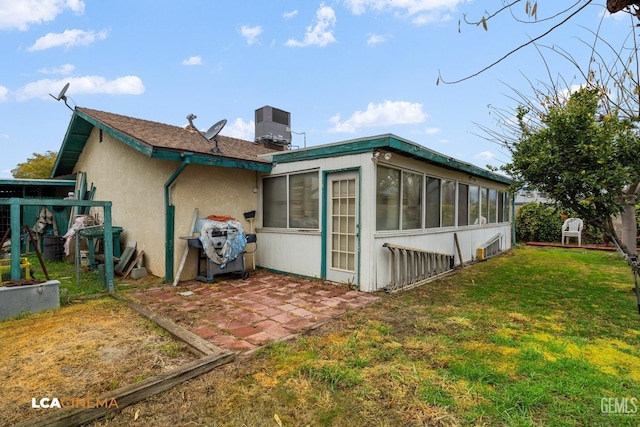 back of property with cooling unit, a sunroom, a lawn, stucco siding, and a patio area