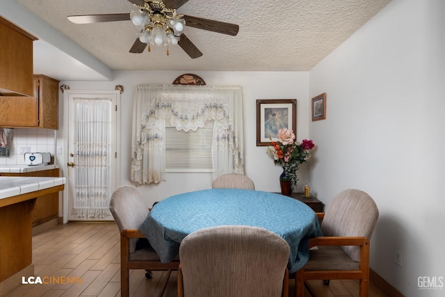 dining space featuring light wood-type flooring, ceiling fan, and a textured ceiling