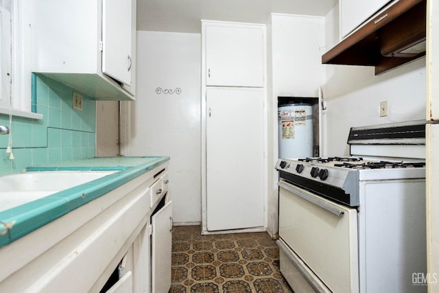 kitchen featuring light countertops, white gas stove, under cabinet range hood, white cabinetry, and backsplash