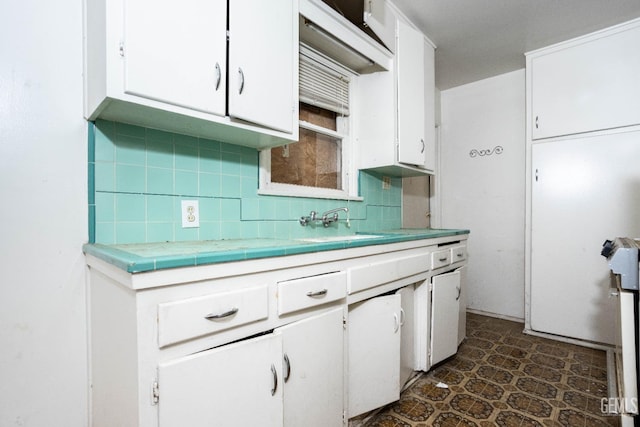 kitchen featuring tile countertops, white cabinets, a sink, and tasteful backsplash