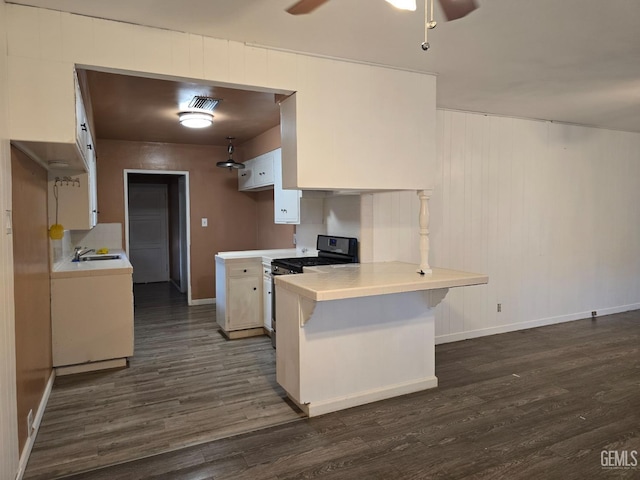 kitchen featuring dark wood-type flooring, gas range, kitchen peninsula, ceiling fan, and white cabinets