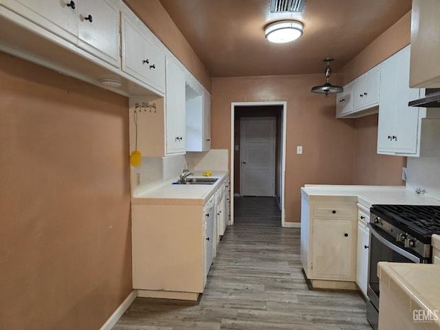 kitchen featuring sink, tile counters, stainless steel range with gas stovetop, and white cabinets