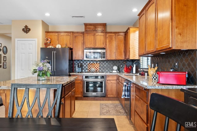 kitchen with a center island, light stone countertops, appliances with stainless steel finishes, tasteful backsplash, and light tile patterned floors