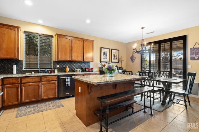 kitchen featuring light stone countertops, light tile patterned floors, stainless steel dishwasher, pendant lighting, and backsplash