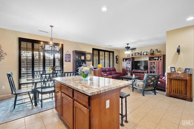 kitchen with ceiling fan with notable chandelier, light stone countertops, a kitchen island, hanging light fixtures, and light tile patterned floors