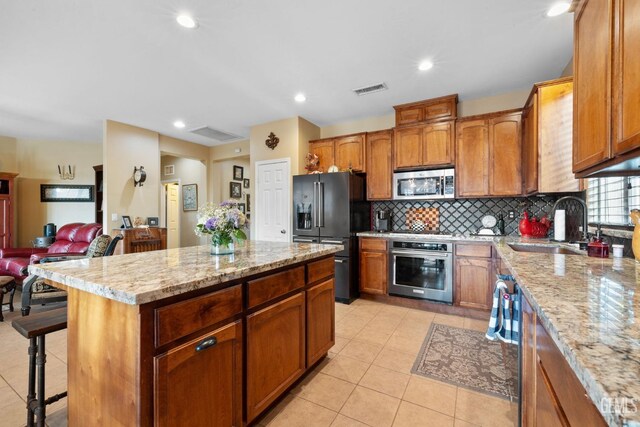 kitchen with light stone countertops, appliances with stainless steel finishes, a center island, decorative backsplash, and sink