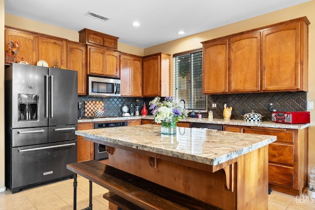 kitchen featuring appliances with stainless steel finishes, a center island, a kitchen breakfast bar, backsplash, and light tile patterned floors