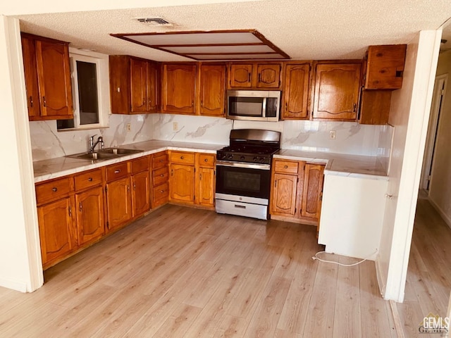 713 18th Pl, Delano, CA 93215 - kitchen featuring stainless steel appliances, brown cabinetry, light wood finished floors, a textured ceiling, and light countertops