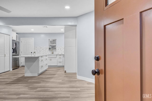 kitchen featuring white cabinetry, stainless steel fridge, light hardwood / wood-style floors, sink, and tasteful backsplash