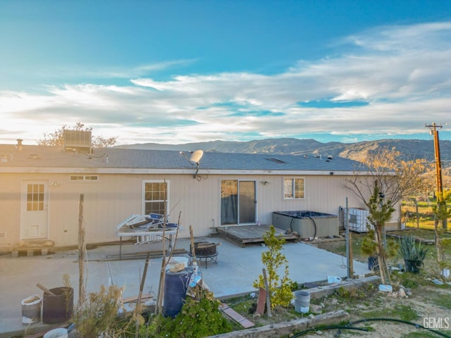 back of property with a mountain view, a patio, a hot tub, and an outdoor fire pit