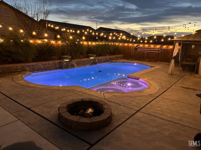 pool at dusk featuring an in ground hot tub, a patio area, and a fire pit