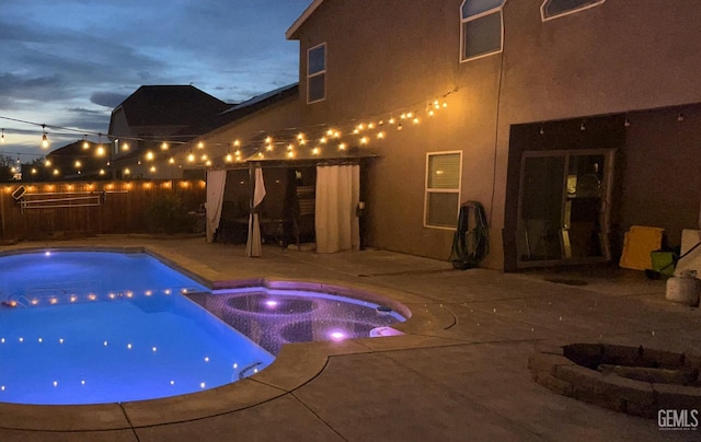 pool at dusk with an in ground hot tub and a patio area