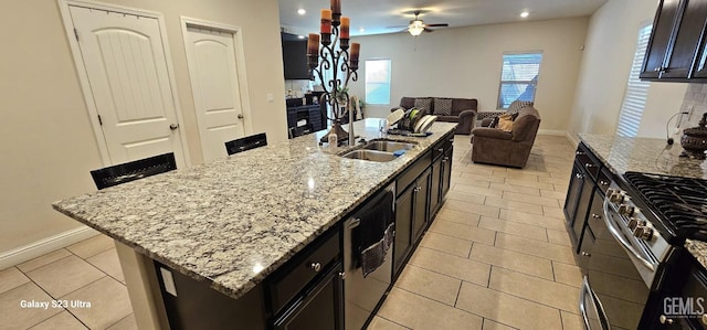 kitchen with sink, light stone counters, light tile patterned floors, dishwashing machine, and an island with sink