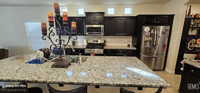 kitchen featuring light stone counters, a kitchen breakfast bar, stainless steel appliances, a kitchen island with sink, and backsplash