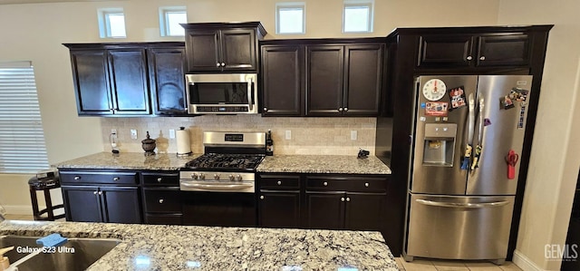 kitchen featuring tasteful backsplash, light stone counters, plenty of natural light, and appliances with stainless steel finishes