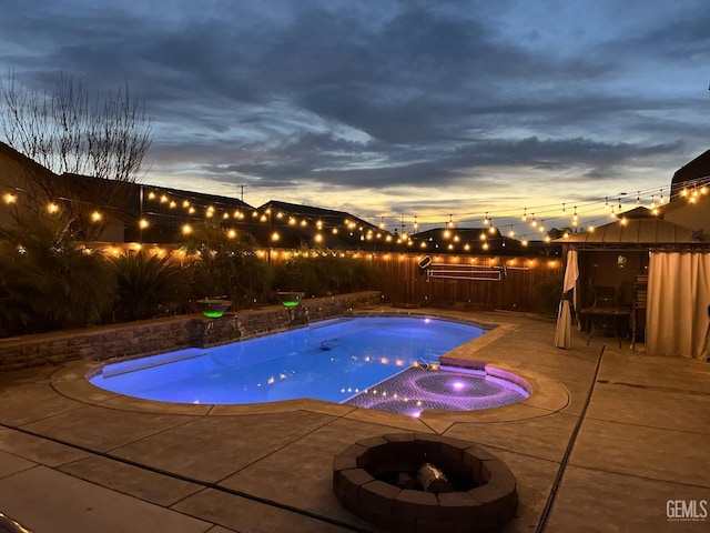 pool at dusk featuring an in ground hot tub, an outdoor fire pit, and a patio area