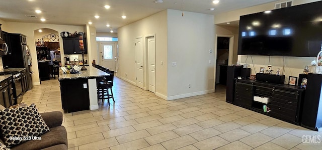 kitchen featuring a center island with sink, light stone counters, stainless steel range oven, a kitchen bar, and light tile patterned flooring