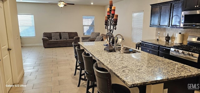 kitchen featuring stainless steel appliances, a breakfast bar, an island with sink, and light stone countertops