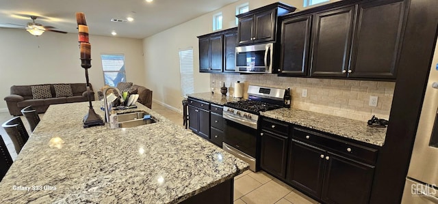 kitchen with an island with sink, sink, backsplash, light stone counters, and stainless steel appliances