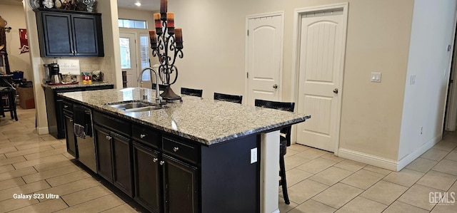 kitchen featuring sink, a kitchen island with sink, backsplash, a kitchen breakfast bar, and light stone counters