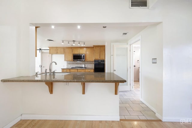 kitchen featuring a kitchen bar, sink, dark stone countertops, appliances with stainless steel finishes, and decorative backsplash