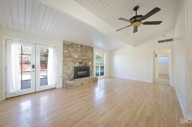 unfurnished living room with wood ceiling, lofted ceiling with beams, light hardwood / wood-style floors, a stone fireplace, and french doors