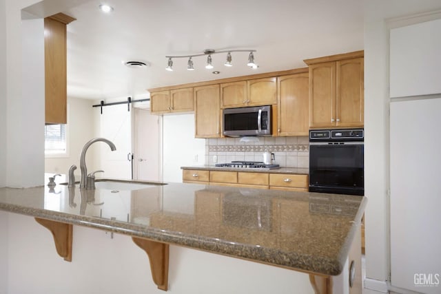 kitchen featuring sink, appliances with stainless steel finishes, dark stone countertops, backsplash, and kitchen peninsula