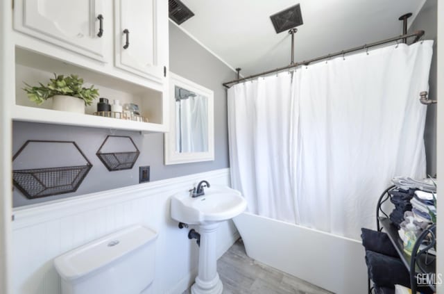 1107 Mcginley Ave, Bakersfield, CA 93308 - bathroom featuring shower / bath combo with shower curtain, wood finished floors, toilet, and wainscoting
