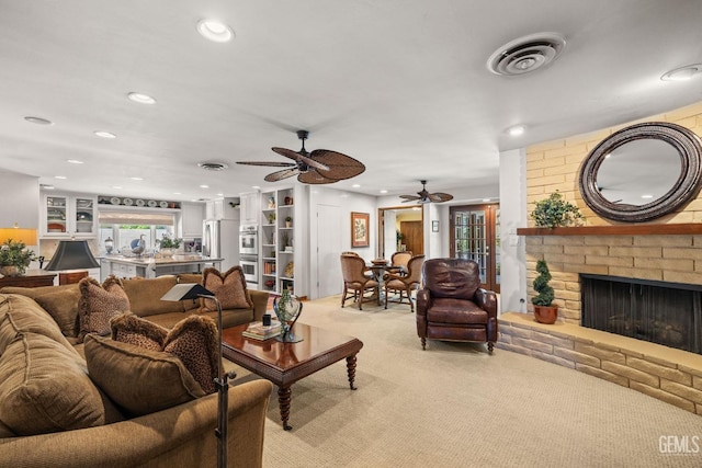 carpeted living room with a fireplace, built in shelves, and ceiling fan