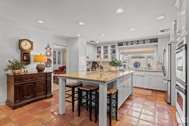 kitchen featuring stainless steel refrigerator, light stone countertops, a kitchen island, a kitchen breakfast bar, and white cabinets