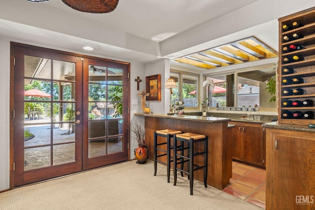 bar featuring dark stone countertops, french doors, light colored carpet, and a healthy amount of sunlight