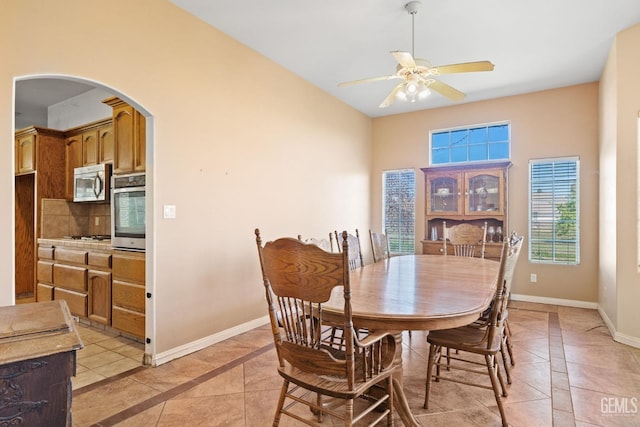 dining room with ceiling fan, baseboards, arched walkways, and light tile patterned flooring