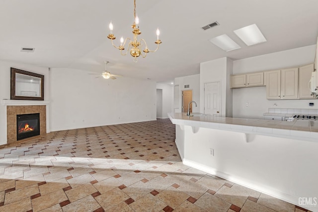 kitchen featuring pendant lighting, a tile fireplace, ceiling fan with notable chandelier, tile counters, and a breakfast bar area