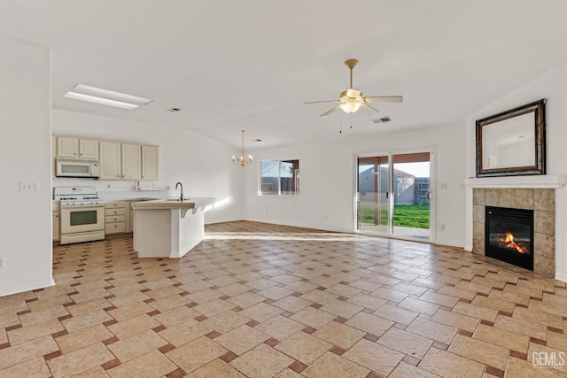 unfurnished living room with ceiling fan with notable chandelier, sink, a tile fireplace, and vaulted ceiling