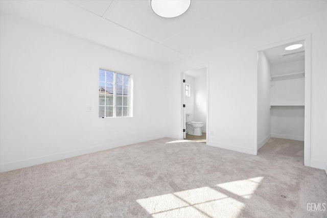 unfurnished bedroom with ensuite bathroom, light colored carpet, a closet, and a spacious closet