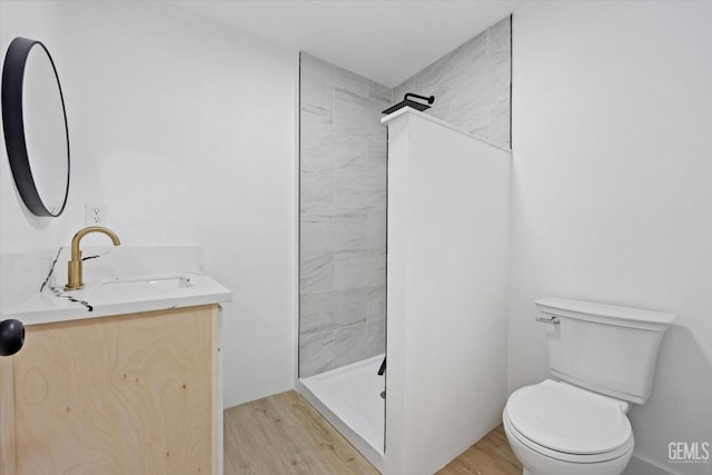 bathroom with toilet, hardwood / wood-style flooring, a tile shower, and vanity