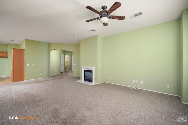 unfurnished living room featuring visible vents, arched walkways, carpet floors, and a glass covered fireplace